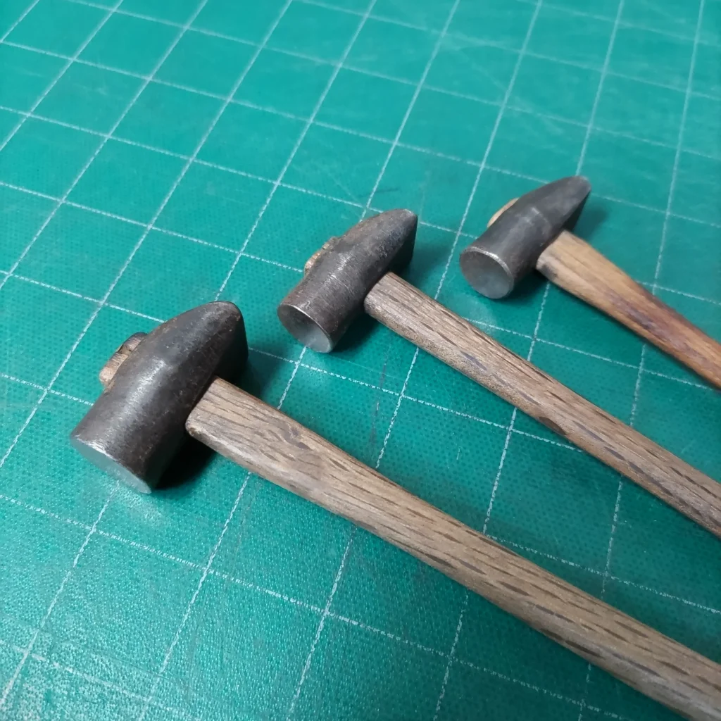 Tres martillos de orfebre de Toru Nishiyama sobre una manta de corte verde.