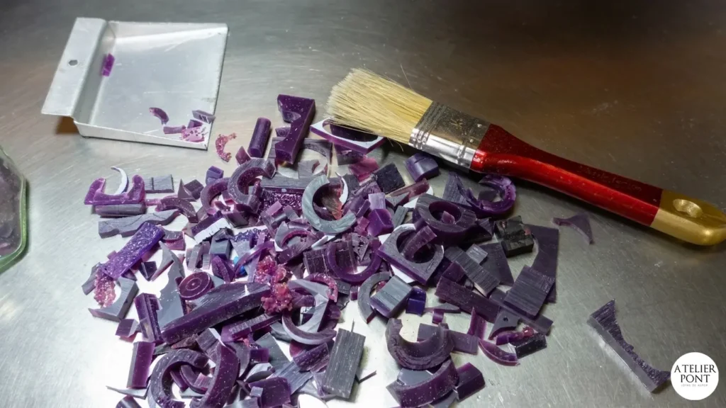 Recortes de cera dura morada y pincel de limpieza en mesa de trabajo de orfebre.