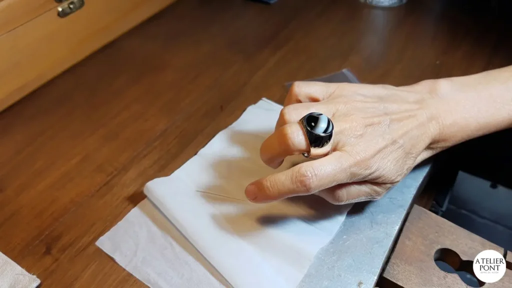 Mano luciendo un anillo de diseño de plata maciza con piedra natural en un taller de joyería.